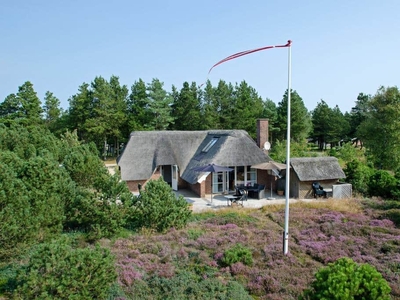 Stort feriehus opført i sten med stråtag beliggende på en stor naturgrund.